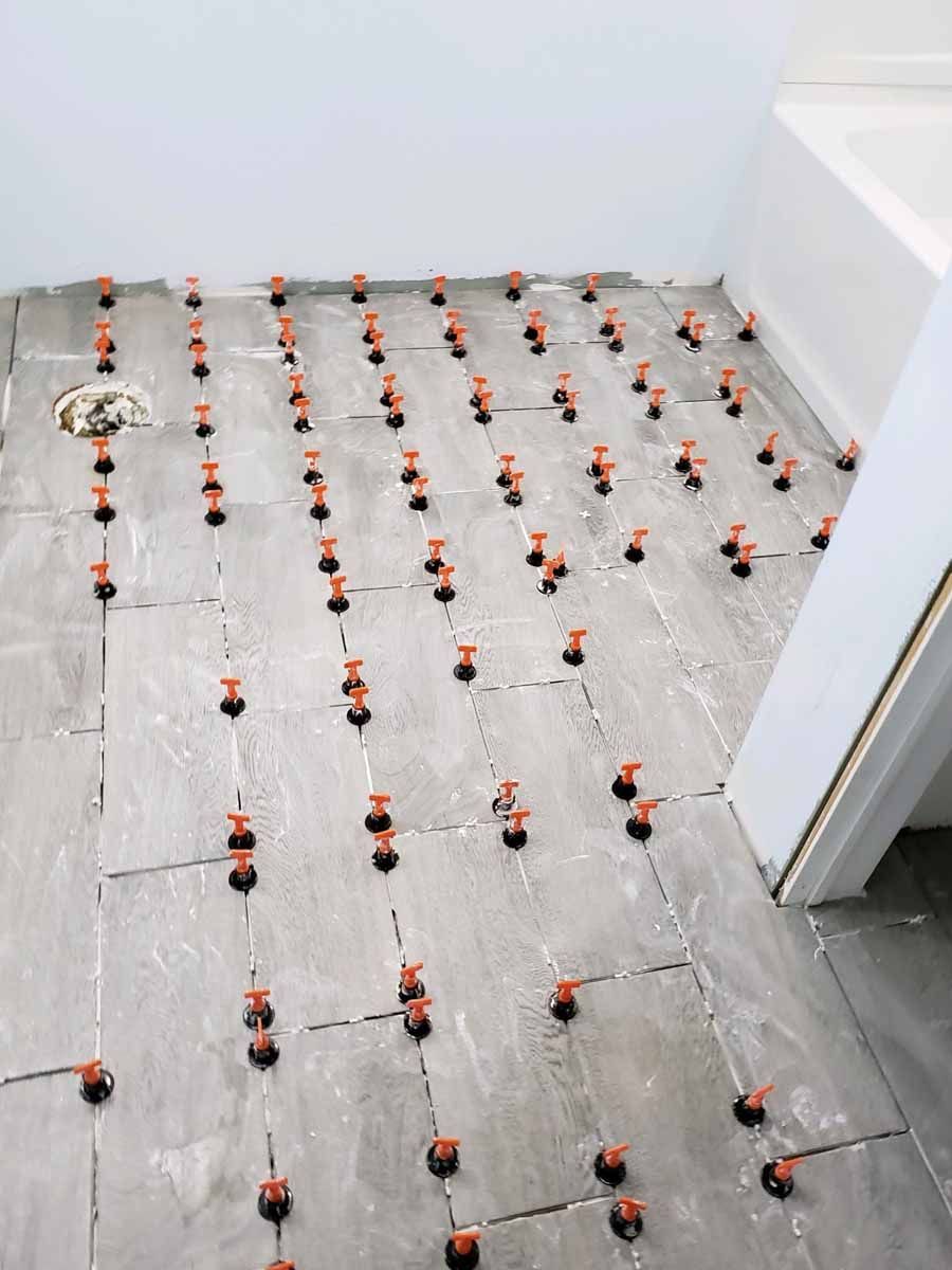 Gray tile flooring with many orange leveling clips set for installation.