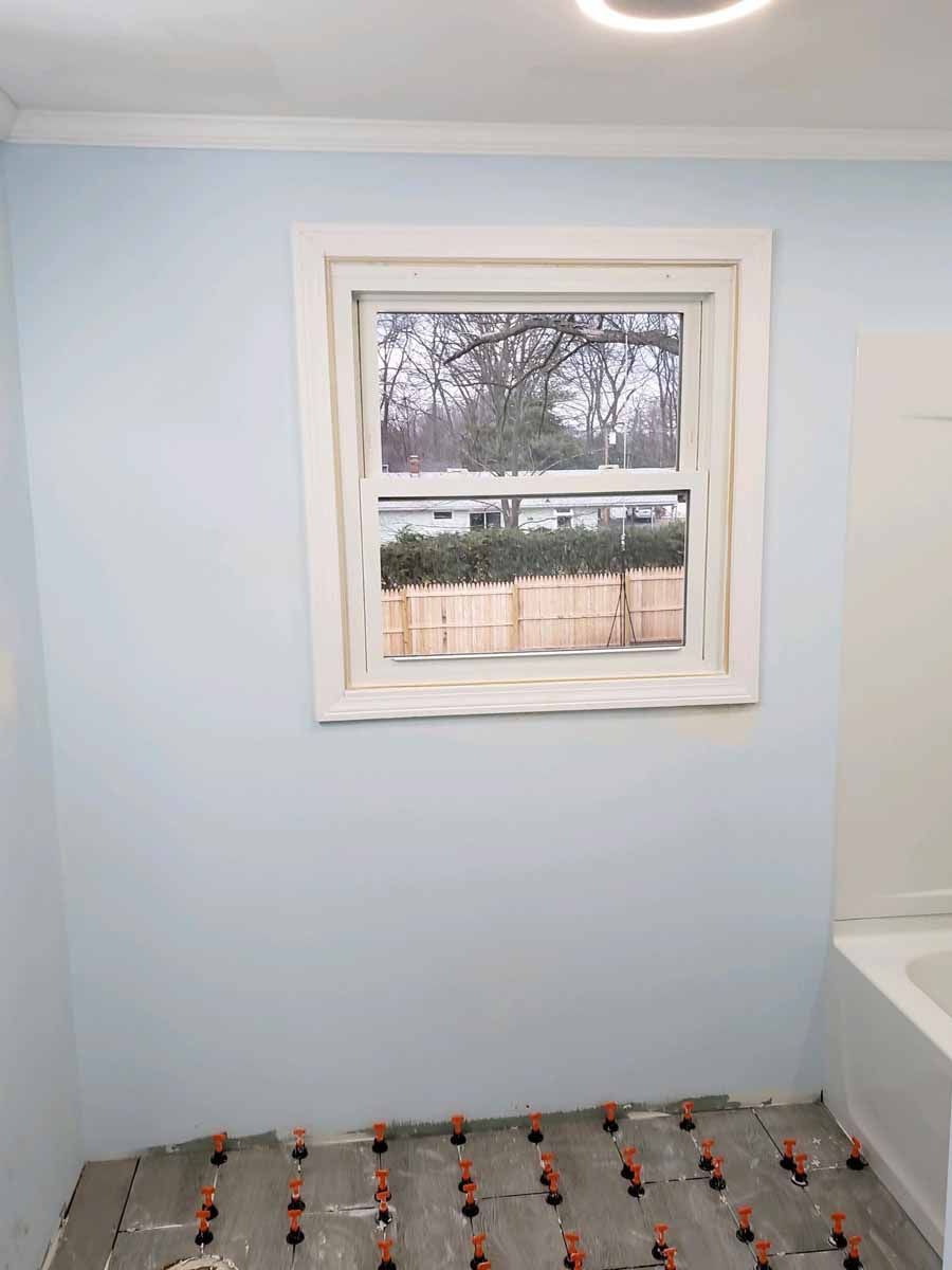 Bathroom with blue walls, a window, and flooring in progress.