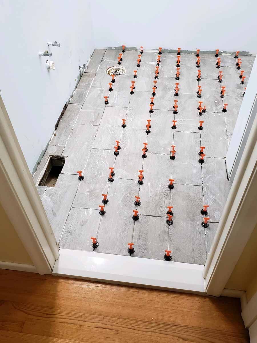 Newly tiled floor in a room, orange leveling clips between tiles.