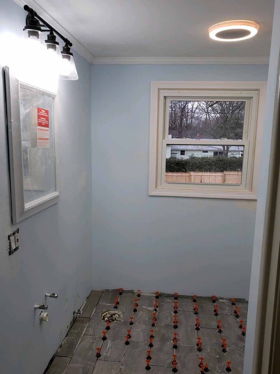 Bathroom under construction with blue walls, window, and tile leveling system on the floor.