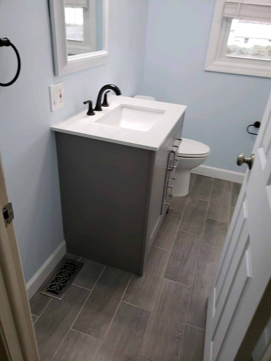 Bathroom with gray vanity, white countertop, white sink, and light blue walls.