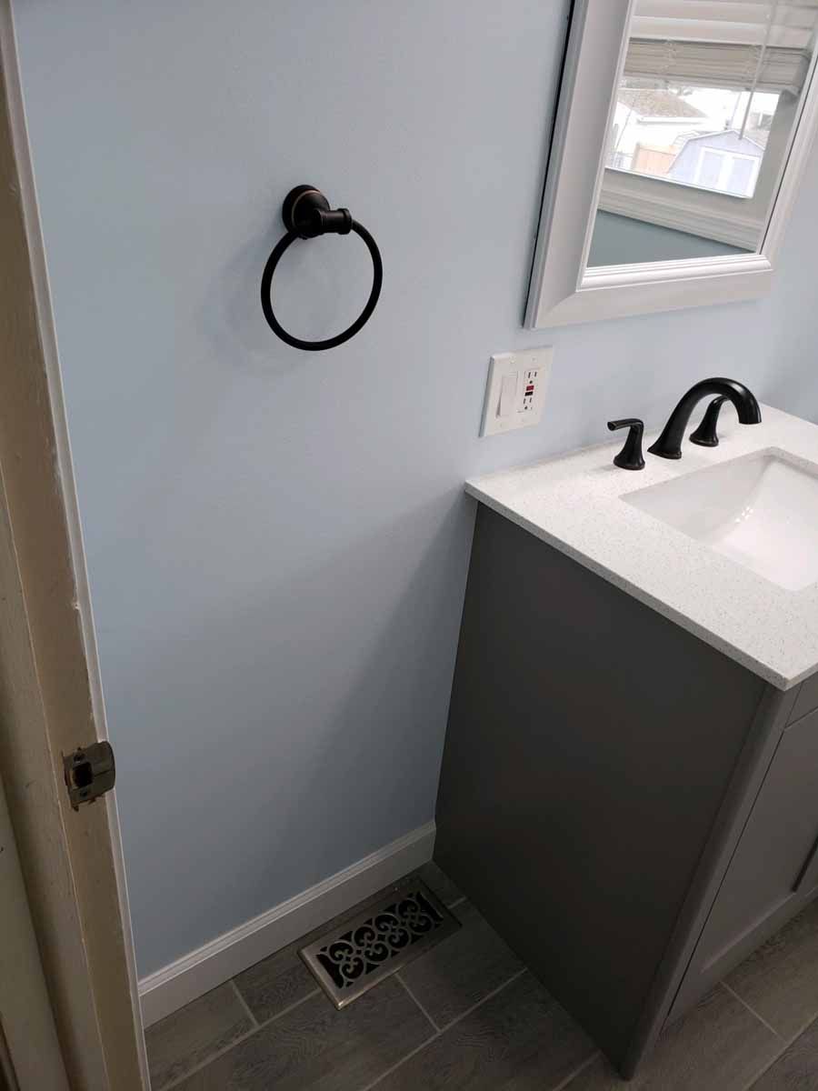 Bathroom with light blue walls, gray vanity, and black fixtures.