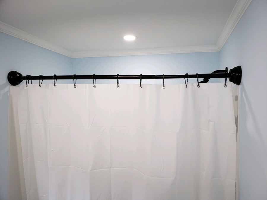 A white shower curtain on a black rod in a light blue bathroom.