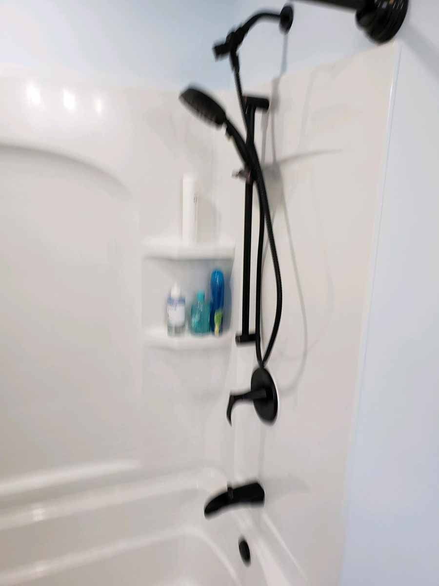 Black showerhead and faucet in a white shower stall with built-in shelf holding toiletries.