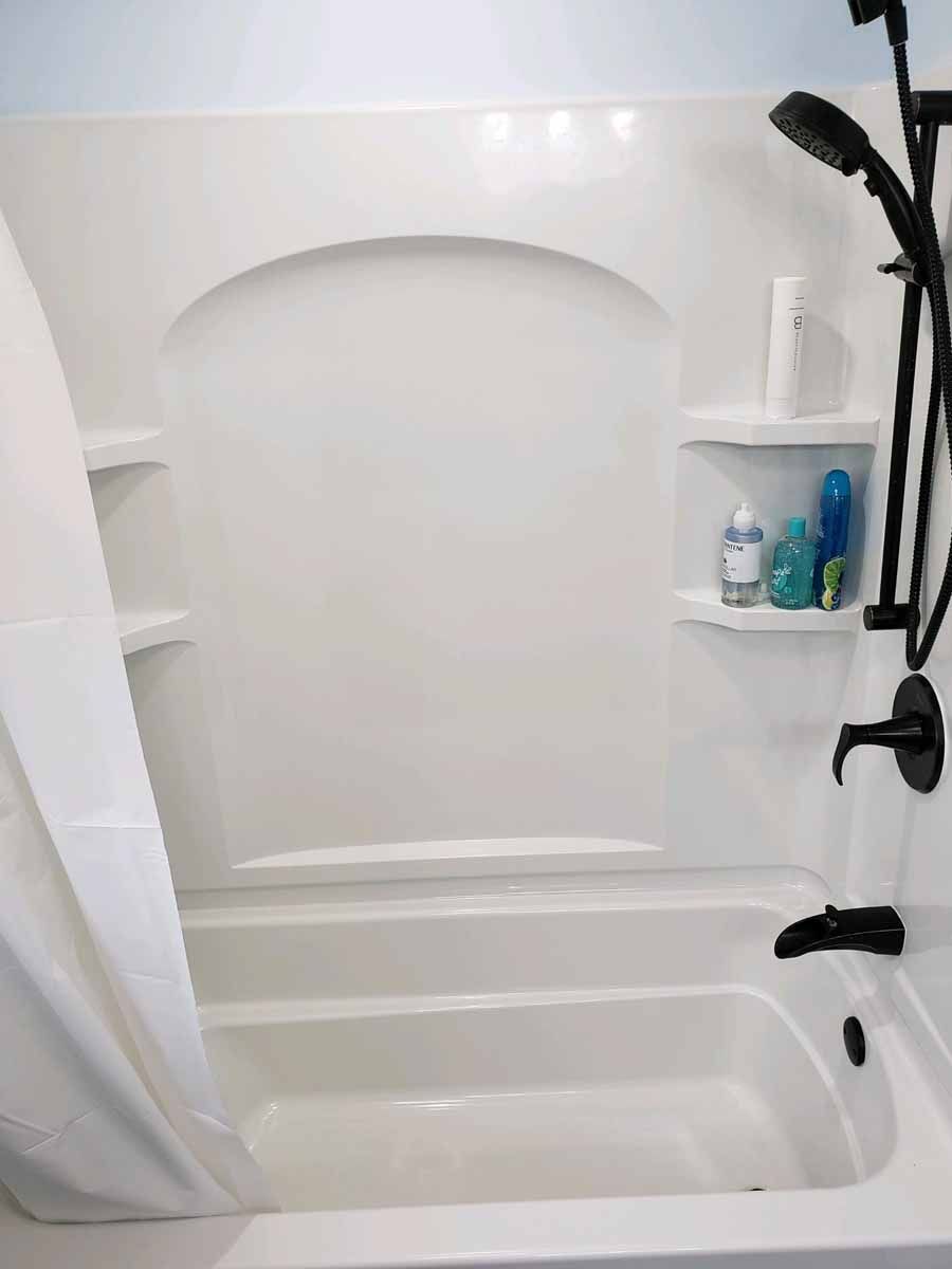 White bathtub and shower combo with built-in shelves. Black shower fixtures and a shower curtain are present.