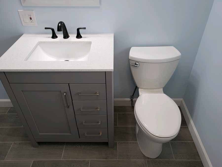 Bathroom with gray vanity, white sink, black faucet, and white toilet on gray tile floor, blue walls.