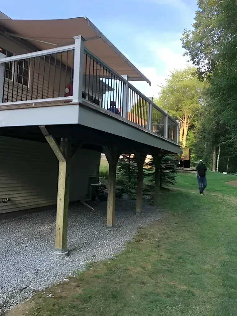 Elevated wooden deck with railing and awning; person walks on grass.