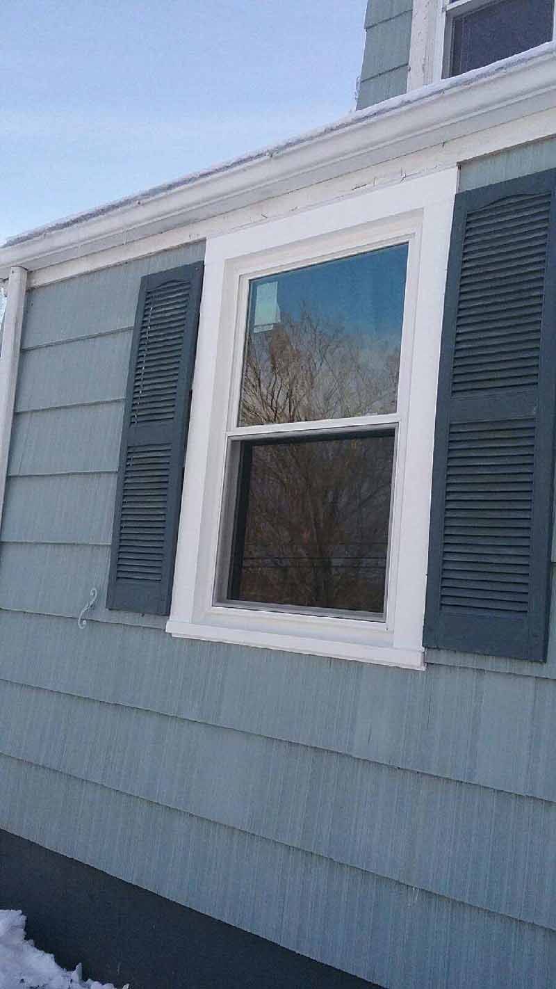 A house exterior with a white-framed window, gray shutters, and light blue siding.