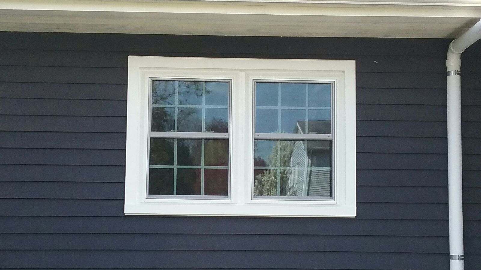 White-framed double-hung window on a dark blue clapboard house. White trim.