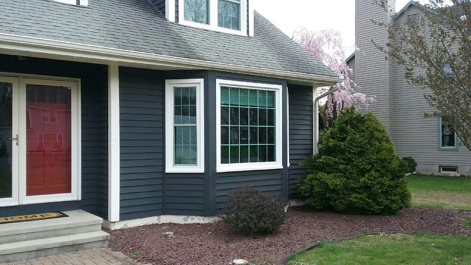Dark gray house with red door, white trim, bay window, and front yard landscaping.