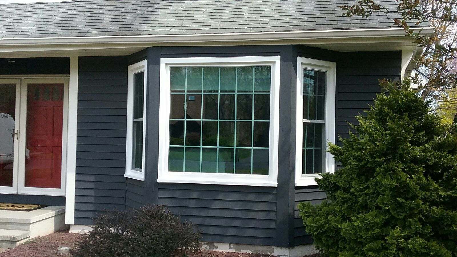 Dark blue house with white trim and a large bay window. Red door on the left, shrubbery on the right.
