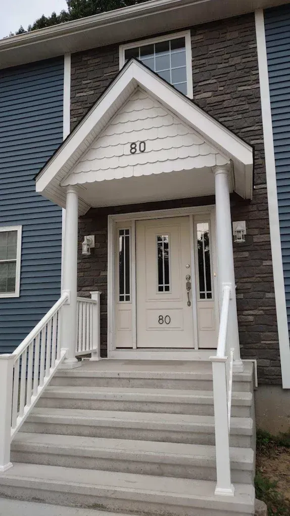 Front entrance of a house with steps, a white portico, and blue siding, with the number 80 on the door.