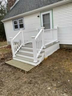 White deck and steps leading to a house entrance. Gray steps and a concrete landing.