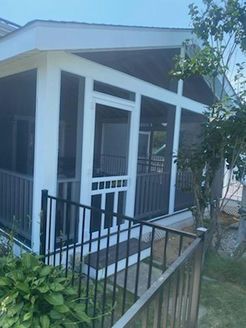 Screened porch with white trim, black railing, and steps leading to the entrance. Lush green plants flank the stairs.