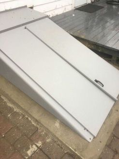 Gray cellar door with sloped sides, leading up to a wooden porch.