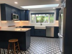Navy blue kitchen with white countertops, stainless steel appliances, and patterned floor.