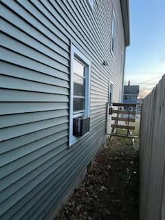 Side view of a two-story building with light blue siding, a window with an AC unit, and a wooden fence.