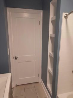 Bathroom with white door, built-in shelving, and blue walls. Tile floor visible.
