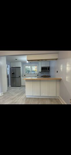 A bright white kitchen with a wooden countertop island, refrigerator, and microwave.