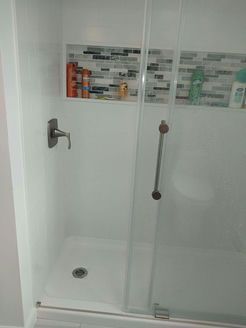 White shower with glass door, mosaic tile shelf with toiletries, and a showerhead.