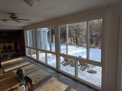 Sunroom interior with a long row of windows overlooking a snowy yard; natural light streams in.