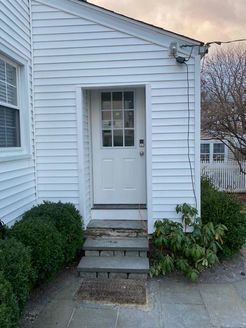 White-sided building with a door, steps, and bushes.