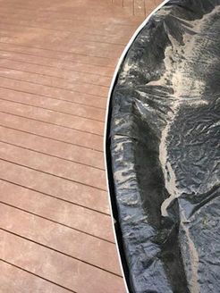 Brown wooden deck next to a black tarp with light-colored debris.