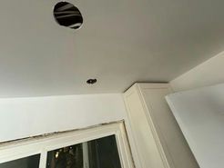 Ceiling with a large hole with wires, small hole, and part of a white cabinet and window.