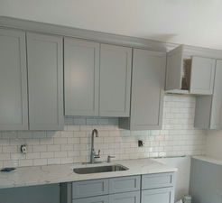 Kitchen with light gray cabinets, white subway tile backsplash, and stainless steel faucet.