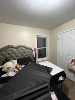 Bedroom with bed, desk, closed door, and window. Black comforter, white desk, and stuffed animals present.