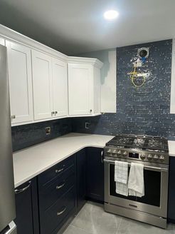 Modern kitchen with navy blue and white cabinets, stainless steel stove, and white countertops.