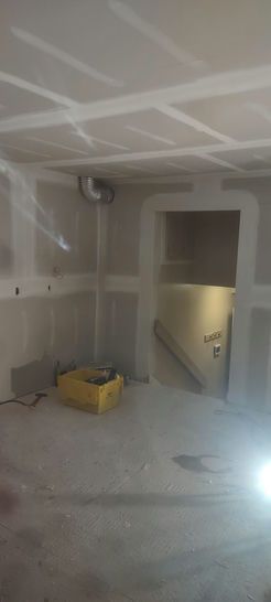 Interior of a room under construction, with exposed drywall, a doorway, and a yellow container.