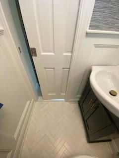 White door slightly ajar in a small bathroom with a vanity and herringbone tile floor.