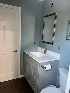 Bathroom with gray vanity, white countertop and sink, silver-framed mirror, toilet, and light blue walls.