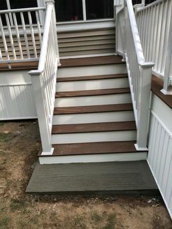 White railing frames exterior wooden stairs leading up to a deck. The stairs have brown treads.