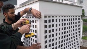 Two people installing lattice fence corner with a power drill.