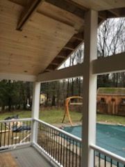 Covered porch with white posts, railing, and wooden ceiling. Pool in the backyard.