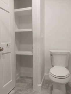 Bathroom with a white toilet, built-in shelving, and a partially open white door.