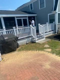 A person standing on a white deck, grilling next to a brick patio and house with a screened porch.
