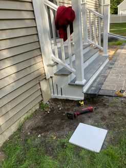 A set of outdoor steps with white railings and gray treads, next to a house with beige siding. Red jacket hangs over railing.