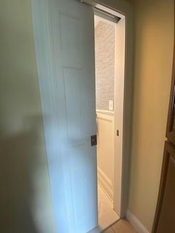 White pocket door open, revealing a hallway. Light-colored walls and flooring.