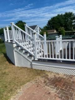 White deck with stairs, gray steps, and lattice detail; outdoors with blue sky.