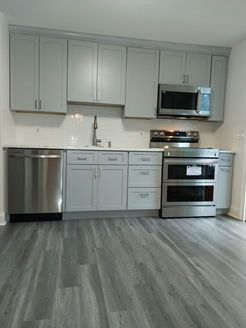 Modern kitchen with gray cabinets, stainless steel appliances, and gray wood-look flooring.