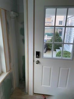 White door with window, partial view of doorway and adjacent wall under construction.