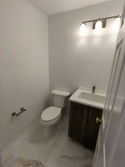 Small white bathroom with a toilet, sink, and dark brown cabinet.