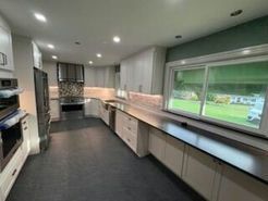 Modern kitchen with white cabinets, dark countertop, large window, and stainless steel appliances.