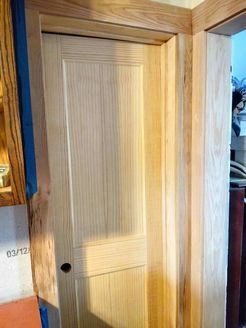 A light-colored wooden door with vertical paneling, inside a wooden frame and trim.