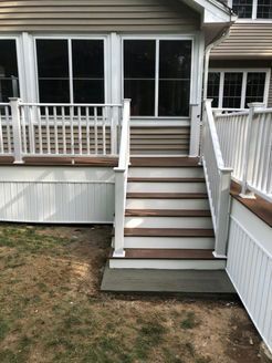 Exterior view of a house with a deck and steps, featuring white railings and brown steps.