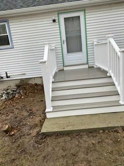 White deck with stairs leading to a back door of a white house. Muddy yard in front.