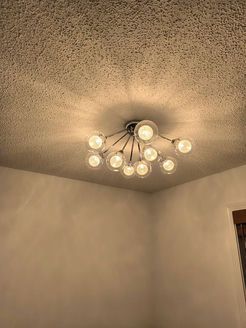 Modern ceiling light fixture with spherical bulbs illuminates a room's corner. Beige walls, textured ceiling.